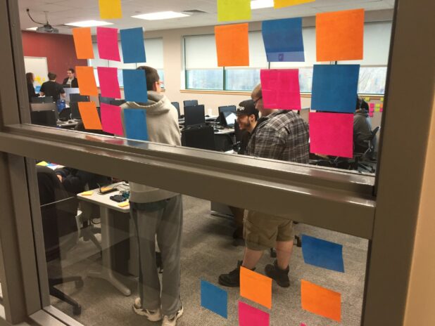 Students seen through a classroom window covered with colorful stickie notes while performing and agile scrum brainstorm