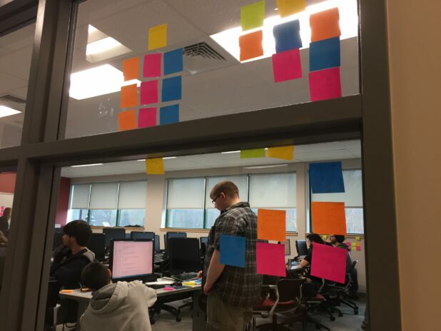 This is a classroom window covered with stickie notes from a agile scrum brainstorm.